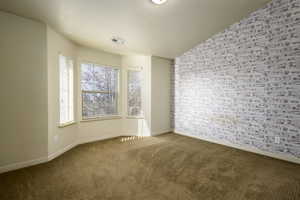 Carpeted primary suite featuring lofted ceiling and brick wall