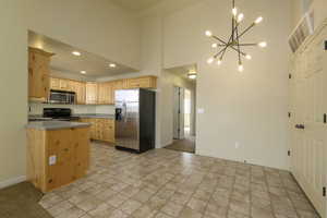 Kitchen with light brown cabinets, a towering ceiling, a notable chandelier, and appliances with stainless steel finishes