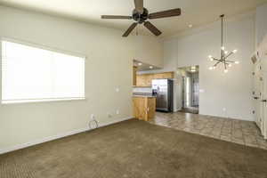 Unfurnished living room featuring light carpet, high vaulted ceiling, and ceiling fan with notable chandelier