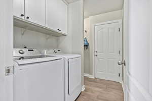 Laundry area with independent washer and dryer, cabinets, and light wood-type flooring