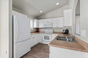 Kitchen featuring lofted ceiling, white appliances, white cabinets, sink, and light hardwood / wood-style flooring