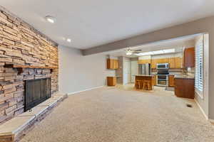 Unfurnished living room with a stone fireplace, light carpet, sink, and ceiling fan