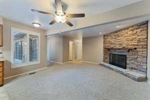 Unfurnished living room featuring light colored carpet, a stone fireplace, and ceiling fan