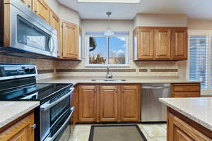 Kitchen featuring light stone countertops, sink, stainless steel appliances, pendant lighting, and decorative backsplash