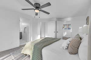 Carpeted bedroom featuring ensuite bath and ceiling fan