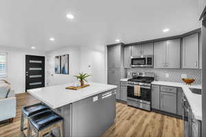 Kitchen with gray cabinetry, a center island, stainless steel appliances, and light wood-type flooring