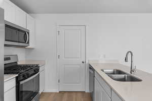 Kitchen with appliances with stainless steel finishes, light wood-type flooring, white cabinetry, and sink