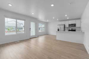 Kitchen with kitchen peninsula, stainless steel appliances, white cabinetry, and light hardwood / wood-style floors