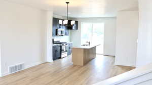 Kitchen with appliances with stainless steel finishes, a kitchen island with sink, sink, pendant lighting, and light hardwood / wood-style flooring