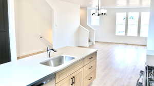 Kitchen featuring light brown cabinetry, light wood-type flooring, sink, pendant lighting, and an inviting chandelier