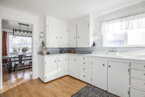 Kitchen with white cabinets, light wood-type flooring, sink, and tasteful backsplash