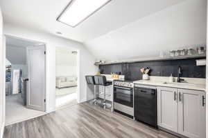 Kitchen with dishwasher, sink, lofted ceiling, stainless steel electric range, and light wood-type flooring