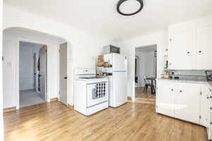 Kitchen with white cabinetry, light wood-type flooring, and white appliances