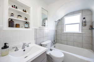 Full bathroom featuring tiled shower / bath, vanity, toilet, and tile walls