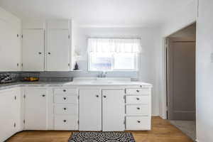 Kitchen featuring decorative backsplash, white cabinetry, sink, and light hardwood / wood-style flooring