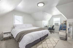 Carpeted bedroom featuring multiple windows, cooling unit, and lofted ceiling