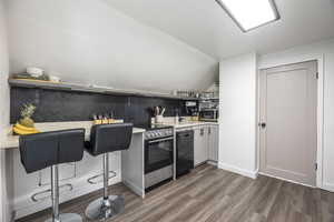 Kitchen featuring hardwood / wood-style floors, white cabinets, sink, vaulted ceiling, and stainless steel appliances