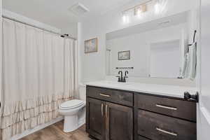 Full bathroom with shower / bathtub combination with curtain, hardwood / wood-style floors, vanity, and toilet