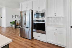 Kitchen with backsplash, white cabinets, stainless steel appliances, and light hardwood / wood-style floors