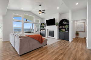 Living room with hardwood / wood-style floors, high vaulted ceiling, fireplace, and ceiling fan