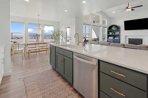 Kitchen featuring dishwasher, sink, ceiling fan, light wood-type flooring, and decorative light fixtures