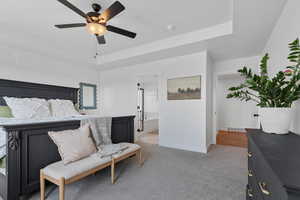 Carpeted bedroom with ceiling fan, a raised ceiling, and connected bathroom