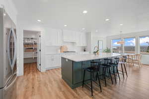 Kitchen featuring white cabinets, stainless steel appliances, decorative light fixtures, and light wood-type flooring