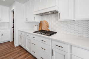 Kitchen with custom exhaust hood, dark wood-type flooring, white cabinets, tasteful backsplash, and stainless steel gas cooktop