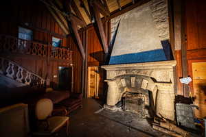 Living room featuring high vaulted ceiling, a stone fireplace, wooden walls, concrete floors, and beamed ceiling