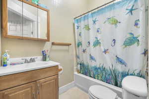 Full bathroom with vanity, shower / bath combination with curtain, toilet, and tile walls