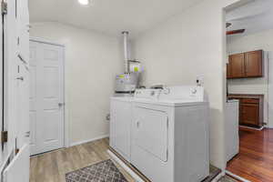 Laundry room with water heater, washer and clothes dryer, ceiling fan, and light wood-type flooring