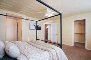 Carpeted bedroom with a textured ceiling, a walk in closet, a closet, and ceiling fan