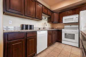 Kitchen featuring light tile patterned flooring, light stone countertops, white appliances, and sink