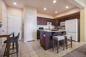 Kitchen featuring a kitchen bar, white appliances, dark brown cabinetry, sink, and a center island