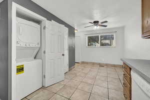 Laundry area featuring ceiling fan, stacked washer and clothes dryer, and light tile patterned flooring