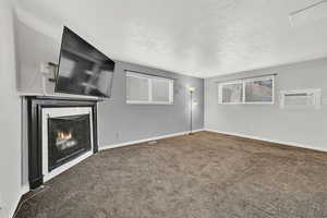 Unfurnished living room featuring a wall unit AC, a tiled fireplace, carpet flooring, and a textured ceiling