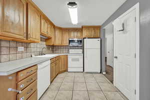 Kitchen with white appliances, sink, light tile patterned floors, and tasteful backsplash