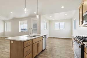 Kitchen featuring a kitchen island with sink, sink, appliances with stainless steel finishes, decorative light fixtures, and light hardwood / wood-style floors