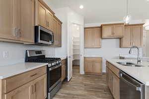 Kitchen with sink, light hardwood / wood-style flooring, decorative light fixtures, and appliances with stainless steel finishes