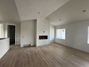 Unfurnished living room with hardwood / wood-style flooring, vaulted ceiling, a textured ceiling, and a large fireplace