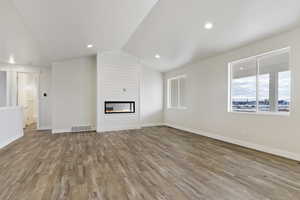 Unfurnished living room featuring a large fireplace, light hardwood / wood-style floors, and vaulted ceiling