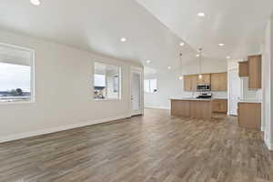 Kitchen with appliances with stainless steel finishes, decorative light fixtures, hardwood / wood-style flooring, lofted ceiling, and an island with sink