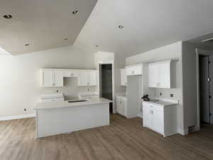 Kitchen featuring lofted ceiling, white cabinets, and a center island with sink