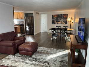 Living room with ornamental molding, a textured ceiling, and dark wood-type flooring