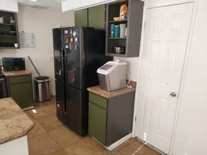 Kitchen featuring black fridge, light tile patterned flooring, and green cabinetry and pantry