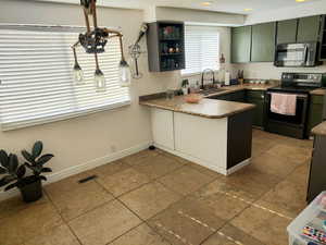 Kitchen with kitchen peninsula, appliances with stainless steel finishes, light tile patterned floors, and integrated sink