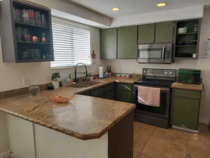 Kitchen with sink, stainless steel appliances, kitchen peninsula, light tile patterned floors, and green cabinetry