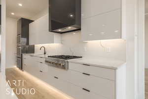 Kitchen with white cabinetry, wall chimney exhaust hood, stainless steel gas cooktop, light hardwood / wood-style flooring, and decorative backsplash