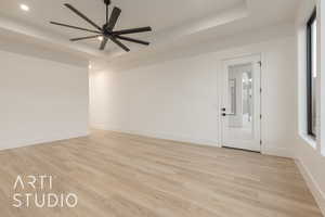 Spare room with a raised ceiling, ceiling fan, and light hardwood / wood-style floors