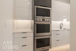 Kitchen with white cabinetry, sink, light hardwood / wood-style flooring, backsplash, and appliances with stainless steel finishes